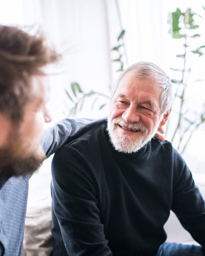 Hipster son and his senior father at home. Two generations indoors, having fun.